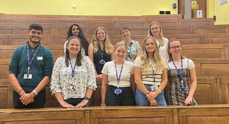 PhD students standing in two rows in lecture theatre.