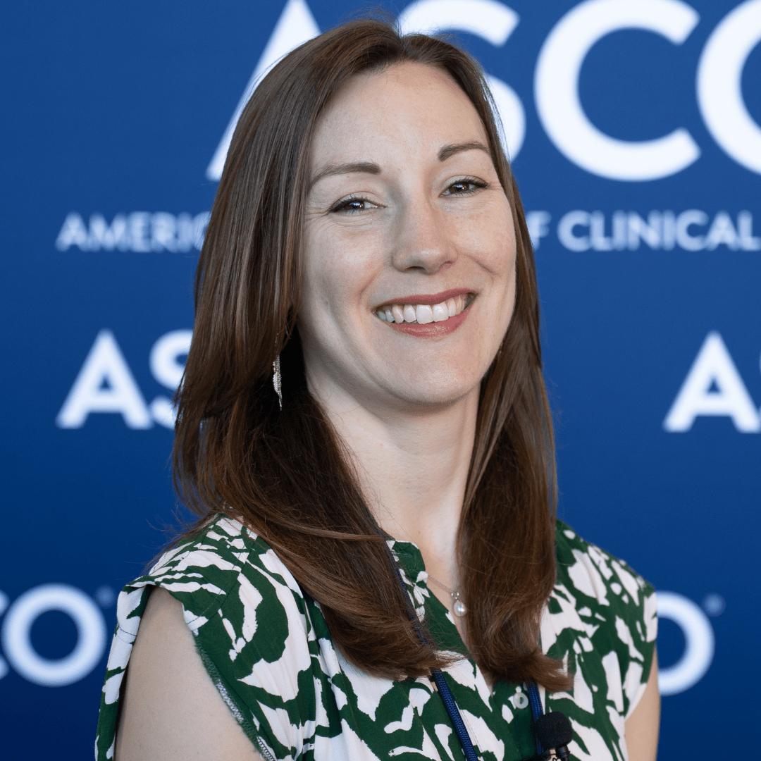 Dr Alison Berner stands smiling in front of a blue conference background